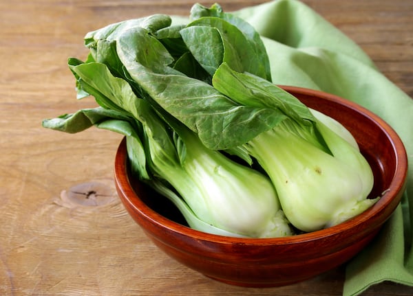 Green and white bok choy heads in a red bowl on a wood table