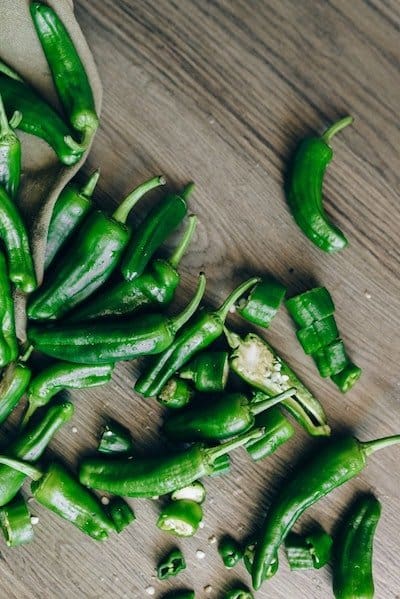 Dark green ripe jalapenos on a brown wooden table, with some cut open to show small white seeds inside