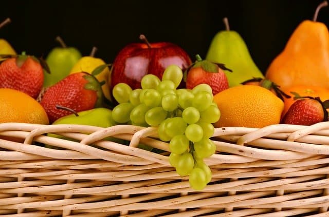 fruit in a basket, including grapes, strawberries, apples, lemons and pears